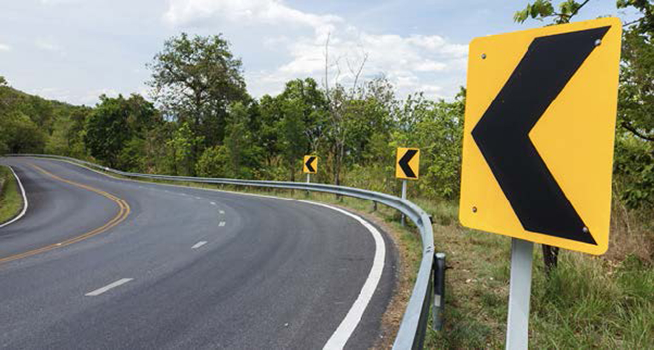 photo of a curved road with three yellow signs with left-pointing arrows