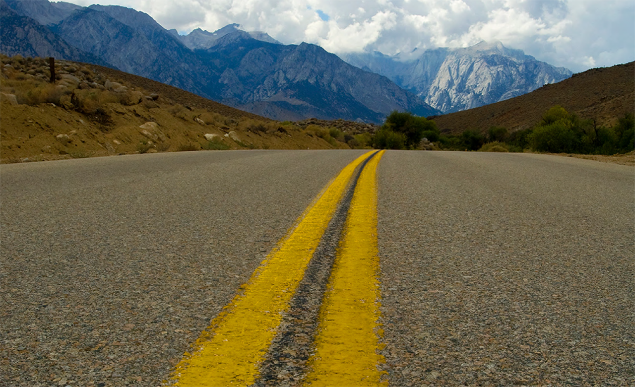close-up photo from Unit 1 of the Road Safety Fundamentals report of a two lane road with mountains in the distance