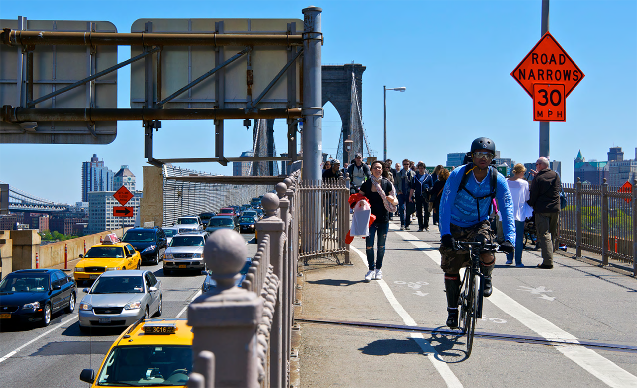 photo from Unit 2 of the Road Safety Fundamentals report showing cars, pedestrians, and a bicyclist crossing the Brookyn Bridge into Manhattan on a sunny day