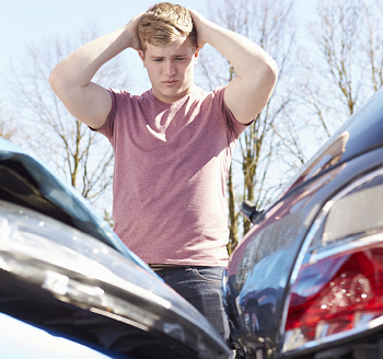teenager with hands on head looking down at the damage done to his car and another car
