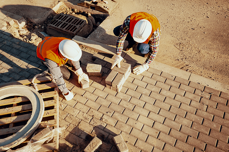 workers arranging paving stones in a sidewalk
