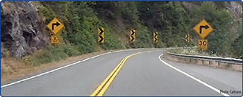 US 199 in Del Norte County on the approach to a horizontal curve with curve warning signs, chevrons, and advisory speed placards. Photo courtesy of Caltrans.