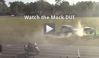 Screen capture from the safety video shows two cars crashing on a high school field. There is a 'play' button graphic atop the photograph to signify that this image is linked to the video.