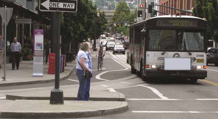 Bus stop with crossing pedestrians in Portland, Ore. (Source: pedbikeimages.org/Laura Sandt) - two pedestrians waiting to cross an intersection by a bus stop